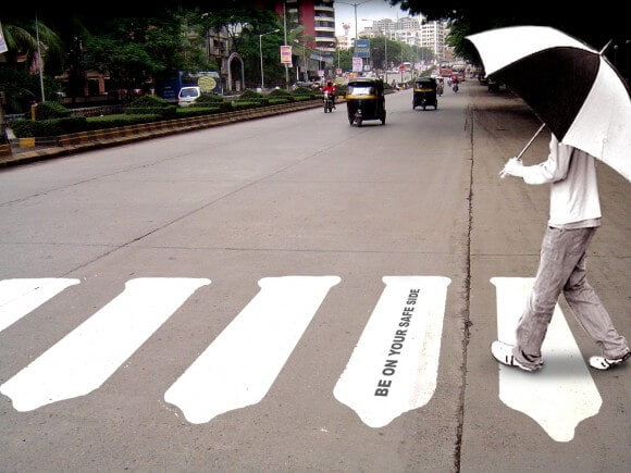 άντρας με ασπρόμαυρη ομπρέλα διασχίζει διάβαση πεζών όπου οι γραμμές έχουν το σχήμα προφυλακτικών
